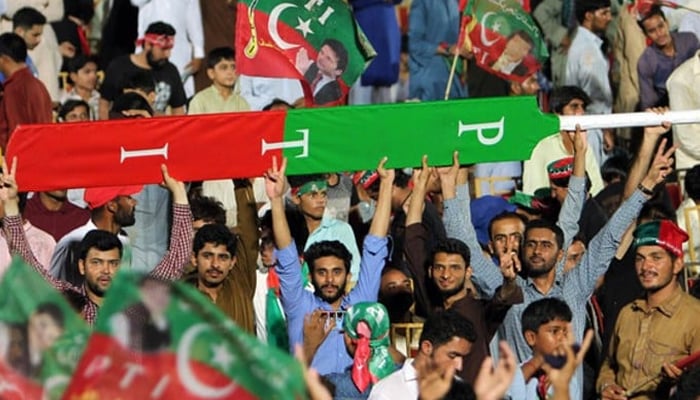 Supporters of former prime minister Imran Khan hold a giant cricket bat with the colors and initials of the party in Multan on July 20, 2018.— AFP