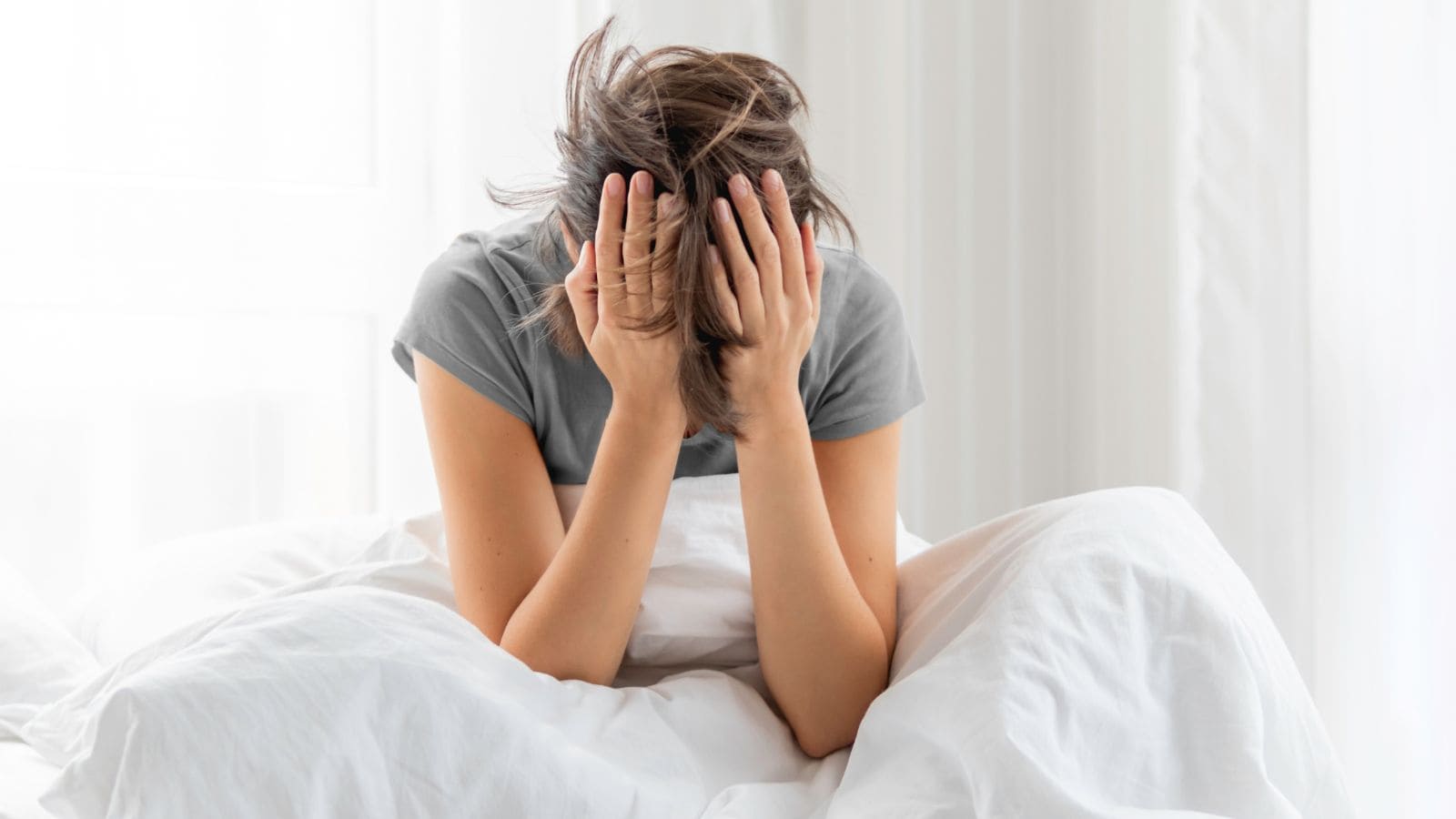 A-sleepy-woman-sits-in-bed-completely-covered-with-a-white-blanket.-The-woman-is-depressed-because-of-Insomnia
